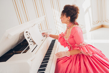 Elegant woman in pink gown playing piano in luxurious historical interior © deagreez