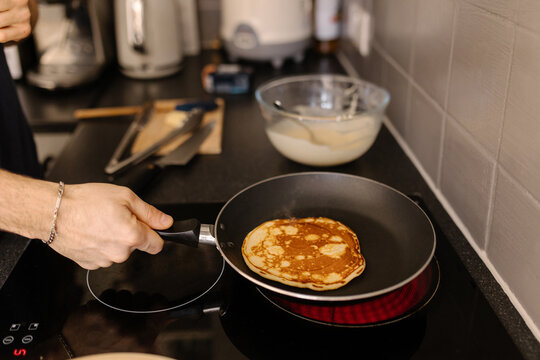 A close-up shot of a man flipping a pancake on a frying pan, soft focus.