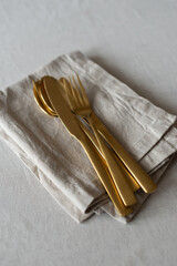 Golden cutlery with beige cotton napkins on the table. Knives, spoons and forks on a neutral cotton...