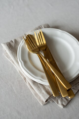 Golden cutlery with beige cotton napkins on the table. Knives, spoons and forks on a neutral cotton...