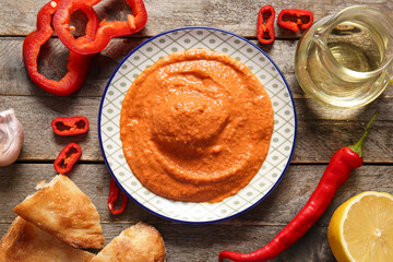Plate of tasty muhammara and ingredients on wooden background