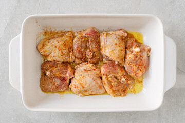  Seasoned raw chicken thighs arranged in a white ceramic baking dish.