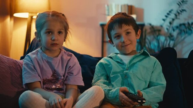 Children's reactions to watching cartoons on TV. Brother and sister watching videos sitting on the couch at home, time spent together is relaxation and happiness. High quality 4k footage