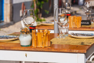 Sunlit outdoor restaurant table set with glassware, menus, and rustic decor