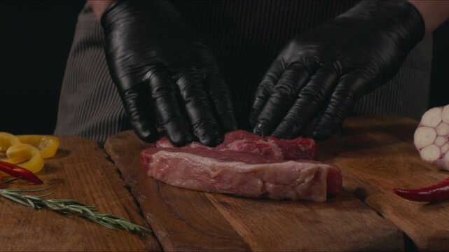 Chef preparing to cooking steak. Raw organic beef meat with rosemary, seasonings, salt and red pepper  on wooden cutting board, close-up. Slow motion