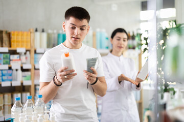 Man chooses skin cream in modern pharmacy. Female pharmacist helps with choosing a medicine
