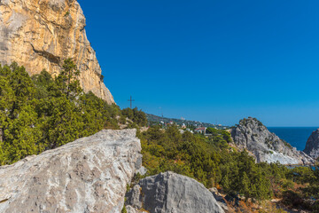 a picturesque view from the southern coast of Crimea. On the left side of the frame rises a powerful steep cliff of a warm golden-yellow hue, covered with light veins. 