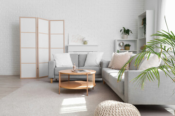 Cozy sofa with cushions, coffee table and folding screen in interior of living room