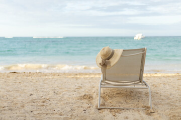 Relaxing beach chair with a sun hat overlooking tranquil ocean waves during a cloudy afternoon on a sandy shore