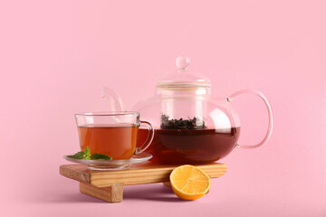 Beautiful composition with glass tea pot, lemon and wooden tray on pink background