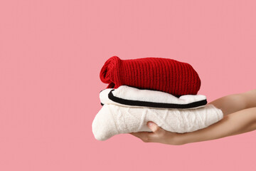 Female hands with stack of warm clothes on pink background