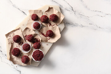 Board with delicious chocolate truffles and torn pieces of paper on light background