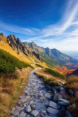 A picturesque hiking path meanders through breathtaking summits, surrounded by golden autumn foliage and a vivid horizon. Discover the beauty of the Western and High Tatras in Slovakia and Poland whi