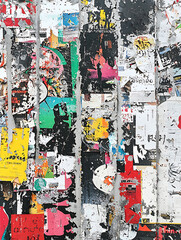 Fototapeta premium Layers of colorful weathered posters create an abstract textured urban surface revealing remnants of past announcements and faded imagery.