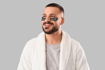 Obraz premium Young man in robe with eye patches on grey background