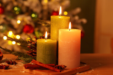 Burning candles and spices on wooden table against Christmas tree in evening