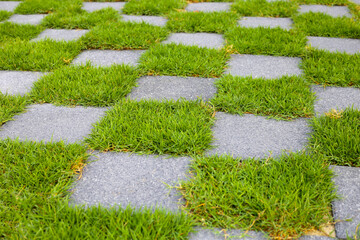 Walkway with a checkerboard pattern, alternating between gray pavement tiles and green grass