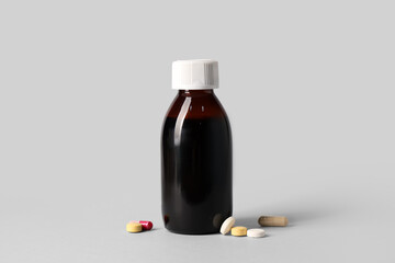 Bottle of cough syrup and different pills on grey background