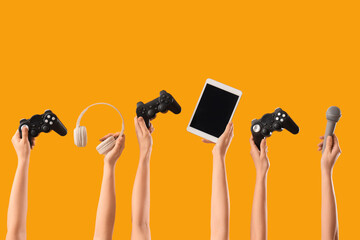 Female hands with game pads, tablet computer, headphones and microphone on yellow background