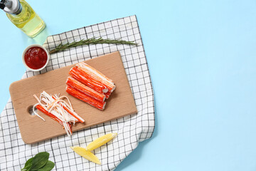 Wooden board with tasty crab sticks, pieces of lemon and bowl of sauce on blue background © Pixel-Shot