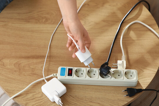 Female hand getting out charger from extension cord on table, top view. National Day of Unplugging