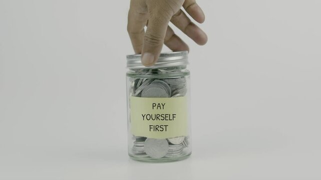 Pay Yourself First text or word on yellow sticky notes attached to a coin jar, hand inserting a coin before sealing the lid, symbolizing prioritizing personal savings before other expenses