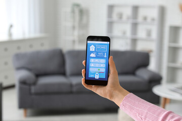 Female hand holding mobile phone with smart home security system control panel in room