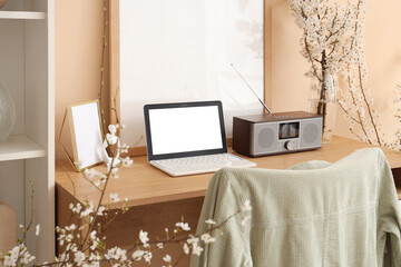 Workplace with modern laptop and blooming branches in vase near beige wall in room, closeup