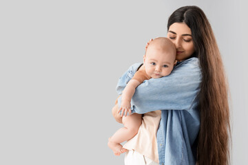 Happy mother holding her little baby on light background