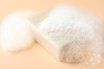 Soap bar with foam on beige background, closeup