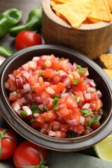 Delicious salsa in bowl, nacho chips and ingredients on table, closeup