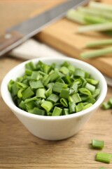 Cut fresh green onions in bowl and knife on wooden table, closeup