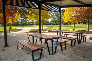 Modern covered picnic area featuring picnic tables and benches under a pavilion.A stylish outdoor dining space offers a public shelter for a community in a suburban neighborhood park in Australia.
