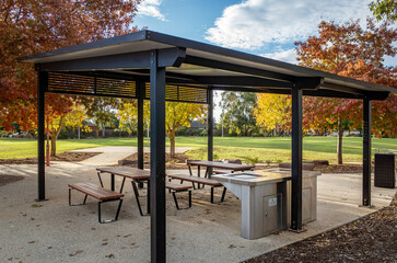 Modern outdoor picnic shelter with sleek black pergola roof, built-in barbecue facilities, and...