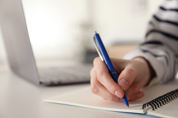 Woman taking notes at white table indoors, closeup. Self-study