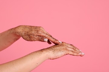 Woman applying body scrub onto her hands on pink background, closeup
