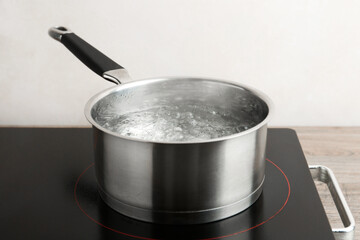 Saucepan with boiling water and stove on wooden table against white background, closeup