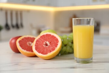Glass of juice and fruits on white marble table in kitchen