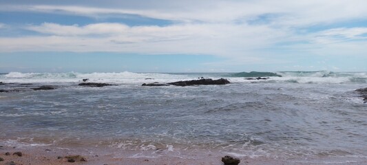 Fototapeta premium Beach with sea rocks, waves, blue sky and clouds