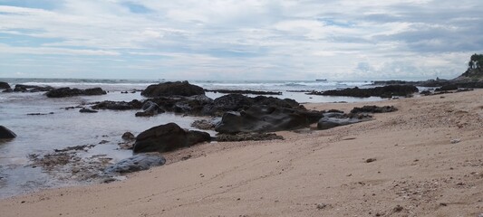 Beach with sea rocks, waves, blue sky and clouds