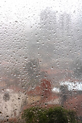 Heavy rain seen through a window with water droplets. The blurred cityscape in the background highlights the visual impact of rainfall during a storm in urban areas.