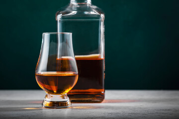 Single malt scotch whisky in glencairn glass with bottle on dark green background