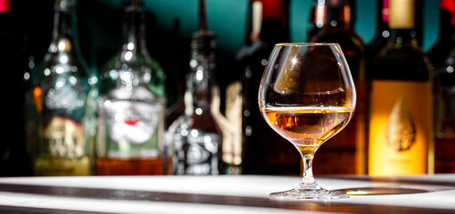 French Armagnac cognac in snifter glass and bottles of strong drinks on dark green background, hard light