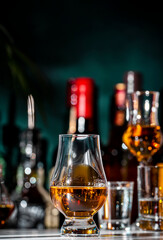 Single malt Scotch whisky in glencairn glass oand bottles of strong drinks n dark green background