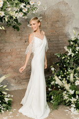 Beautiful young girl bride in her hands with a bouquet in a wedding dress at the arch