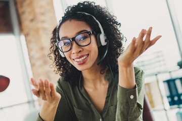 Young businesswoman wearing a headset at an office desk smiling professionally, representing...
