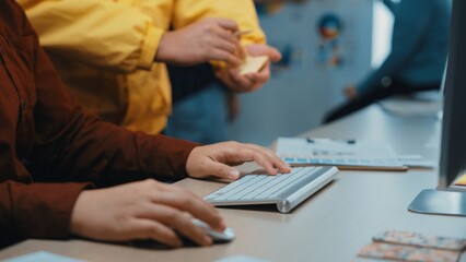 A detailed close-up view of creative professionals working together in a bright office space, showcasing their hands on a keyboard and colorful sticky notes. SACTR