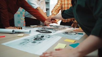 A dynamic creative team engages in a brainstorming session, hands together over design sketches and notes, showcasing collaboration and innovative ideas in an office setting. SACTR