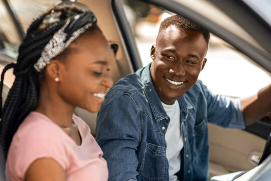 Excited afro american couple travellers looking at map while driving cozy car, side view, copy space. Happy millennial black man and woman checking map before starting journey, sitting in auto - Powered by Adobe