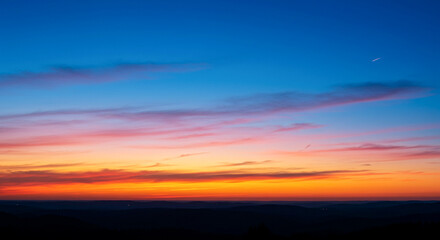 Fototapeta premium A vibrant sunset paints the sky with fiery colors above a dark, silhouetted mountain range. The scene captures the tranquility and beauty of nature at dusk.